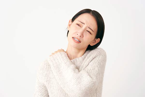 A woman in a sweater holds her shoulder in pain.