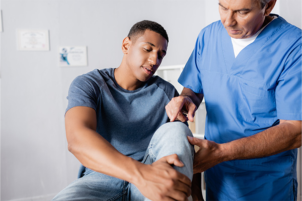 A patient holds his knee up for a doctor to look at.