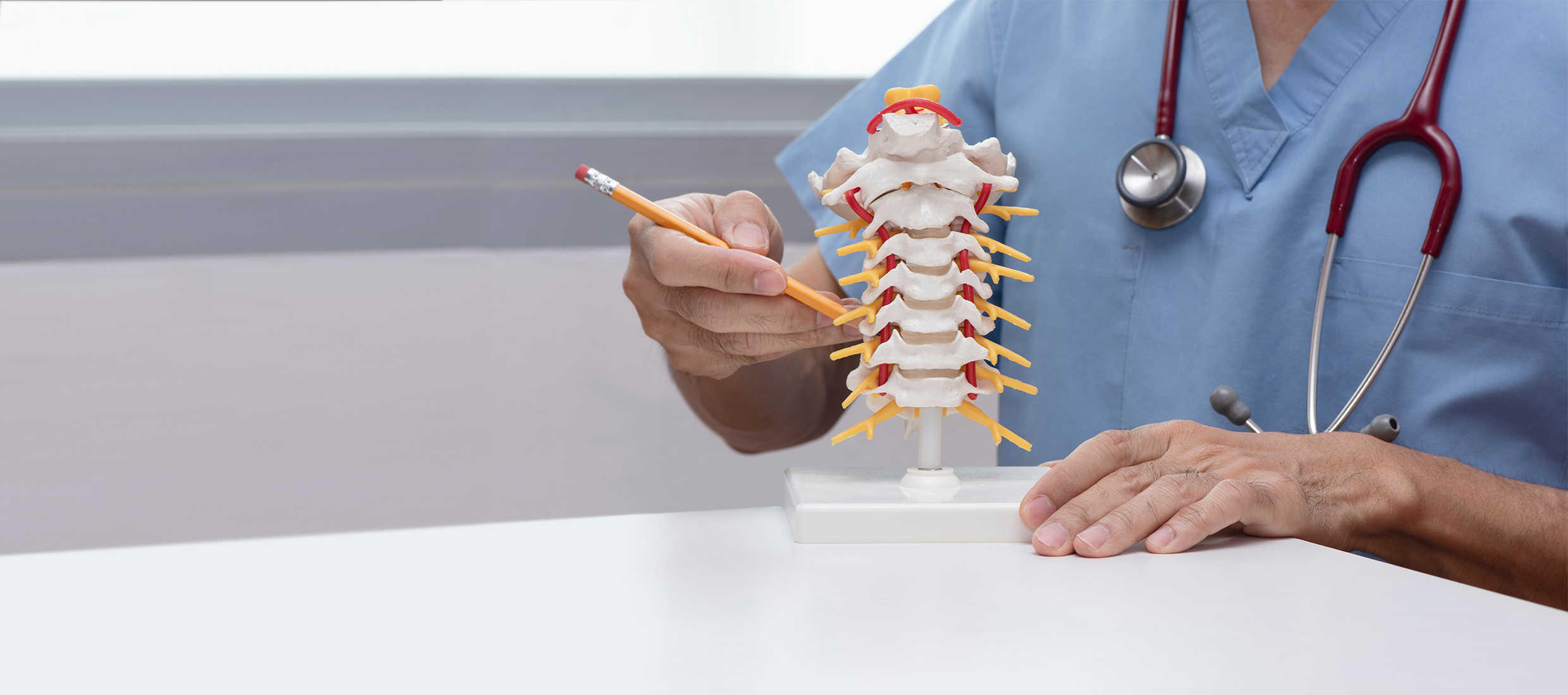 A male Keck Medicine spine doctor with a stethoscope points to a model of a spine with a spinal cord injury