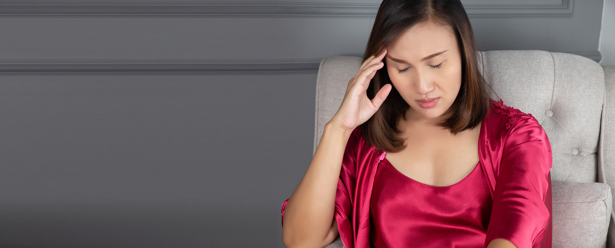 A woman with a headache sits in a chair and touches her head