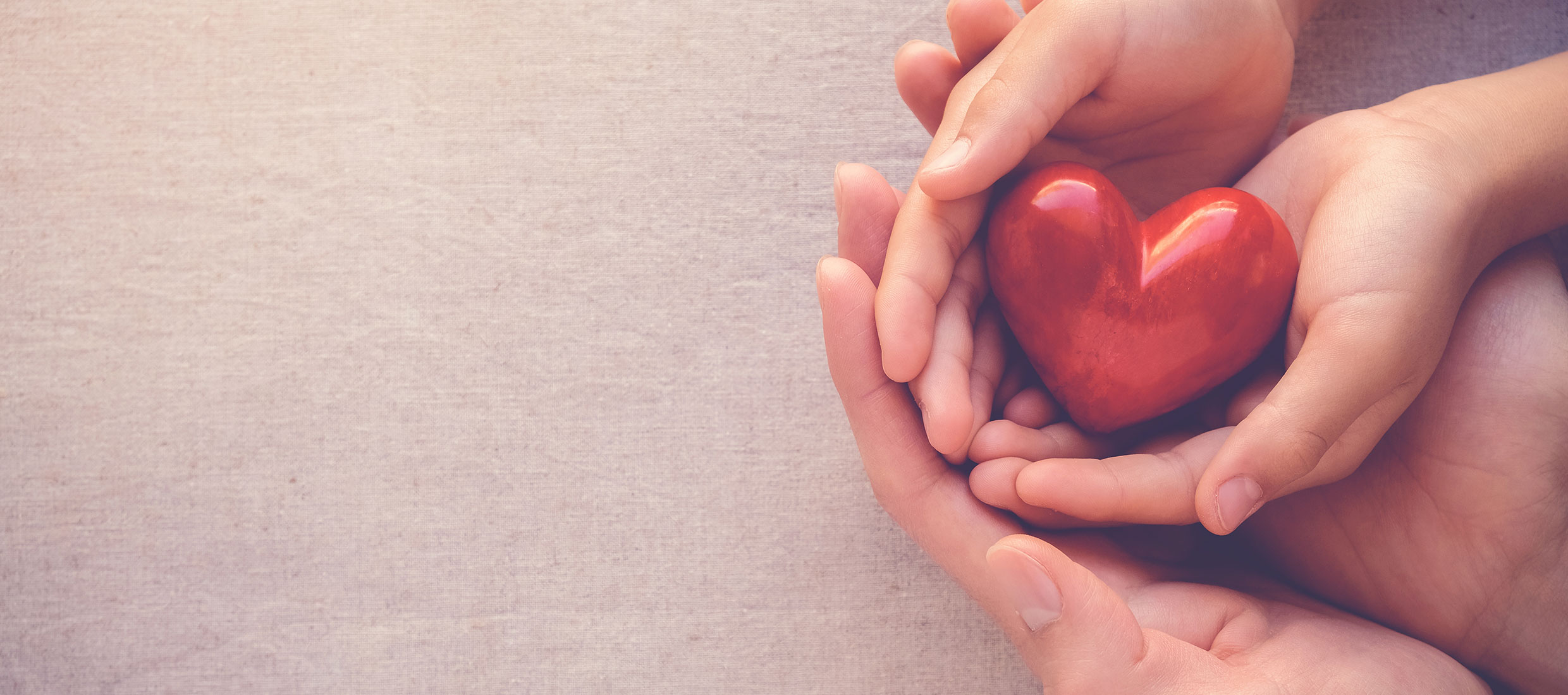 Two pairs of nested hands gently hold a red heart