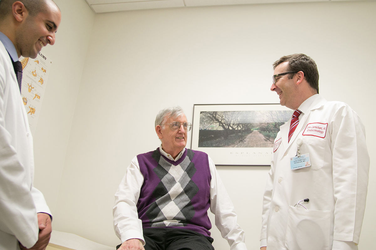 Two male Keck Medicine of USC neurosurgeons smile and talk to a senior male patient in a medical office setting