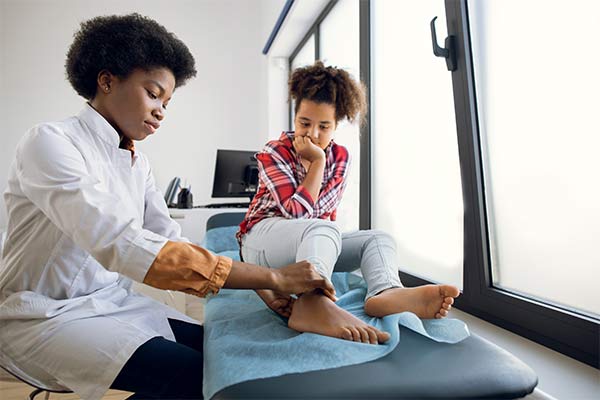 A teenage girl sits on the examining table at modern clinic while a doctor examines her leg.