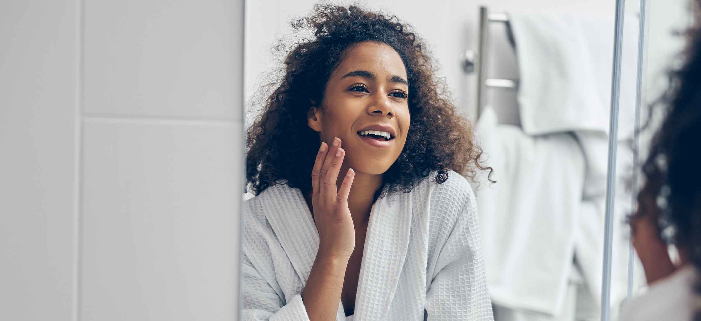 A woman looks into the mirror and touches her cheek.