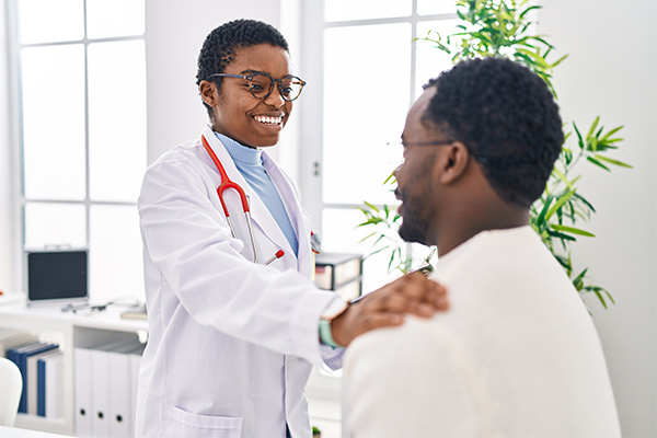 A man and woman doctor and patient have a medical consultation with her hand on his shoulder at a clinic.
