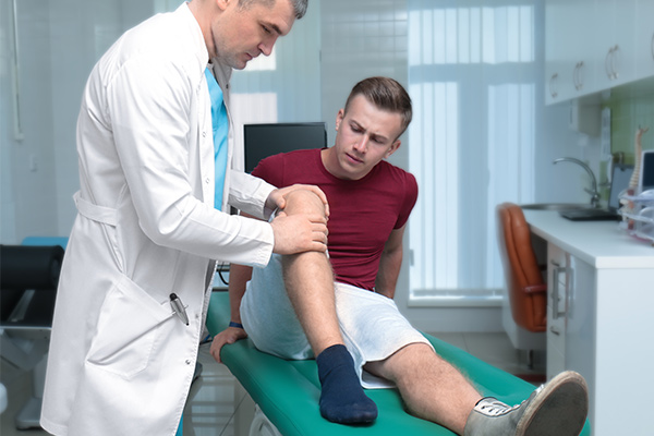 A doctor holds a mans knee as he sits on a medical table.