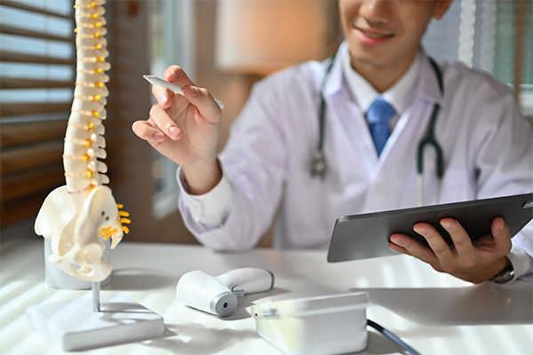 A spine surgeon points to an anatomical model of a spine.