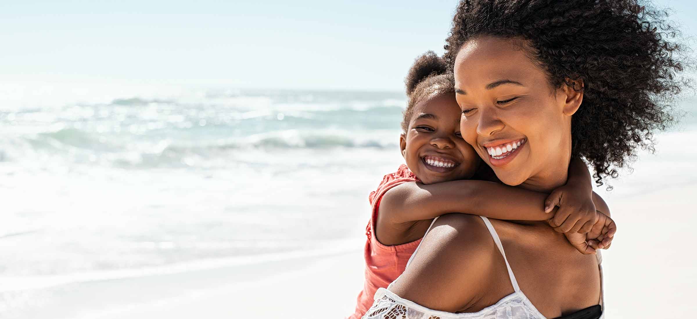 Smiling young black mother and beautiful daughter having fun on the beach.