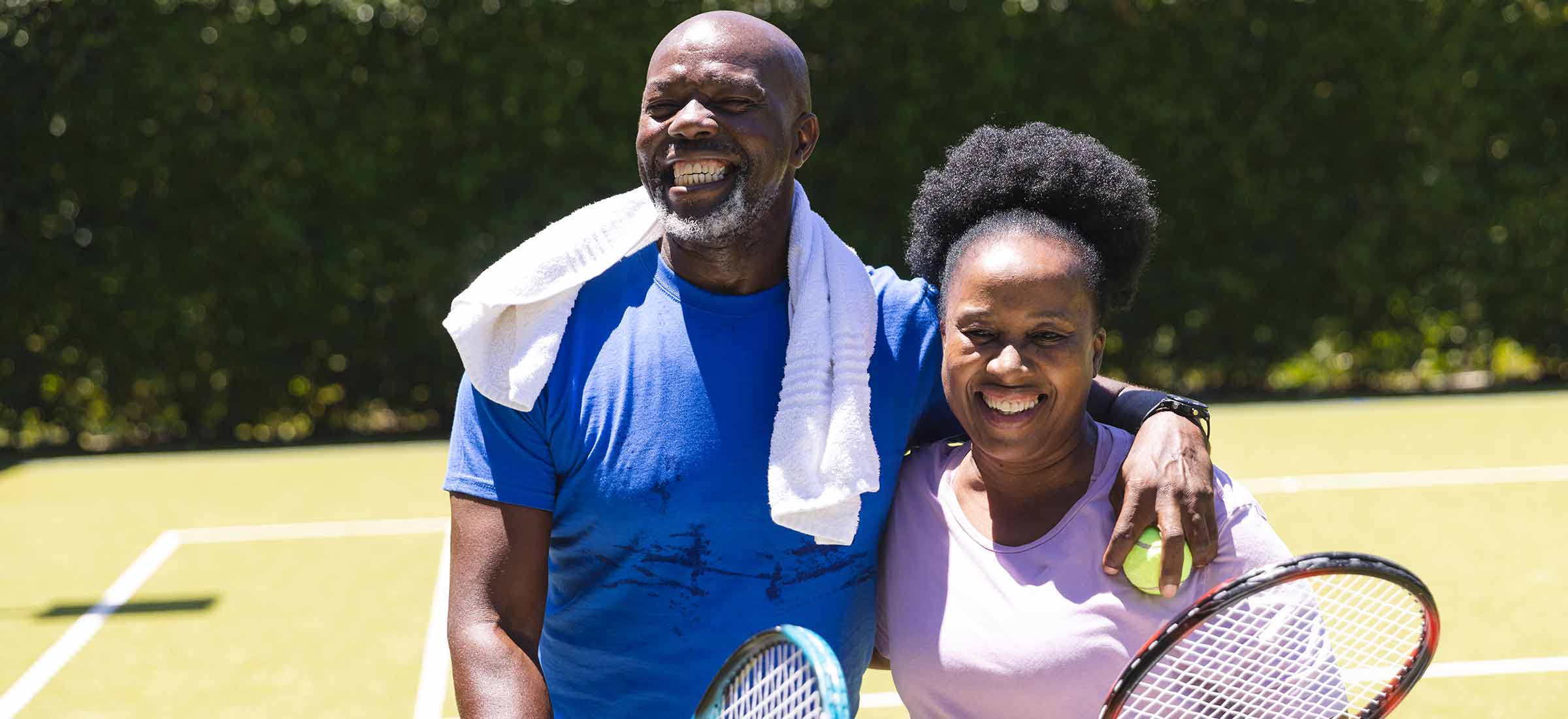 A man and a woman stand together on a tennis court smiling.