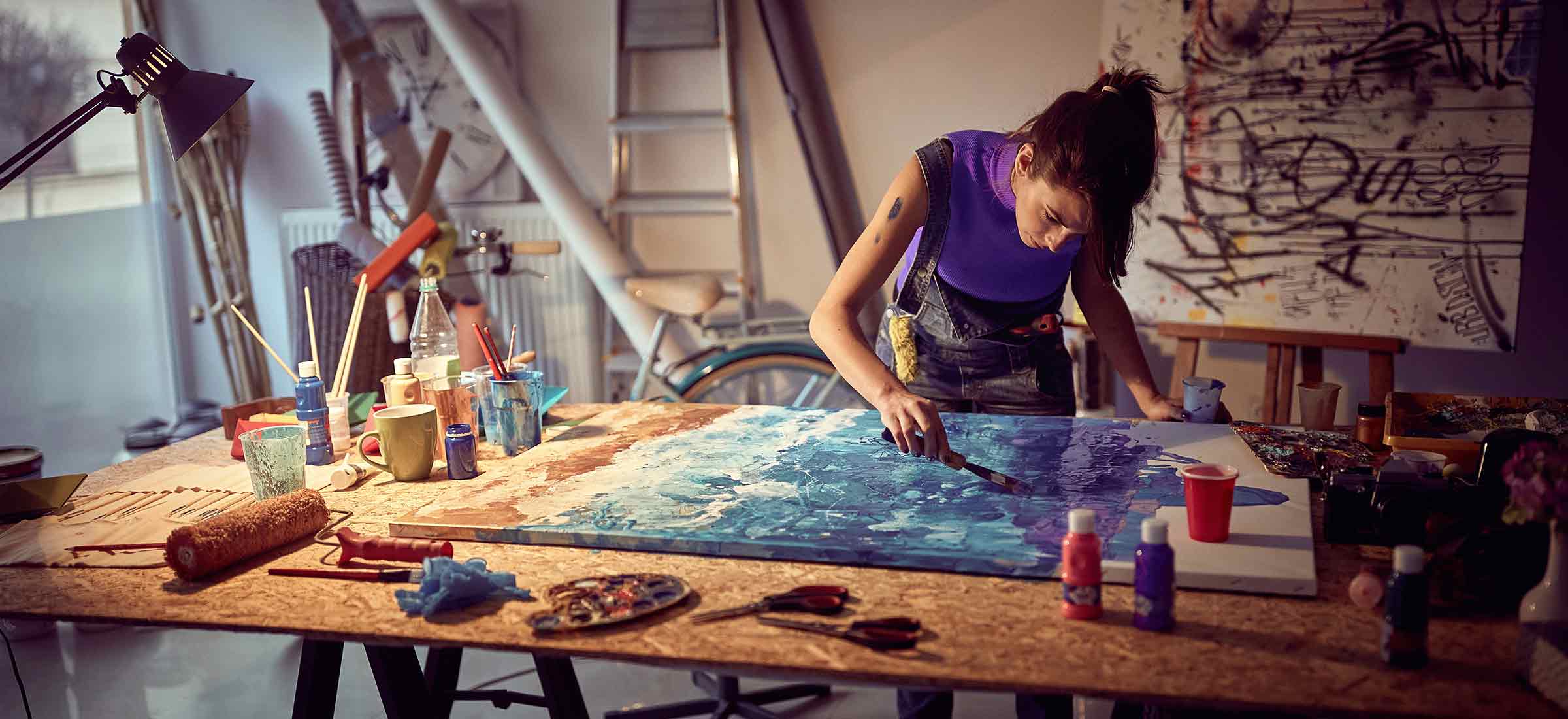 A woman works on a painting in a studio.