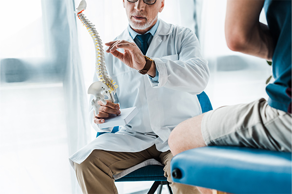 A cropped view of man sitting near doctor gesturing while holding spine model.