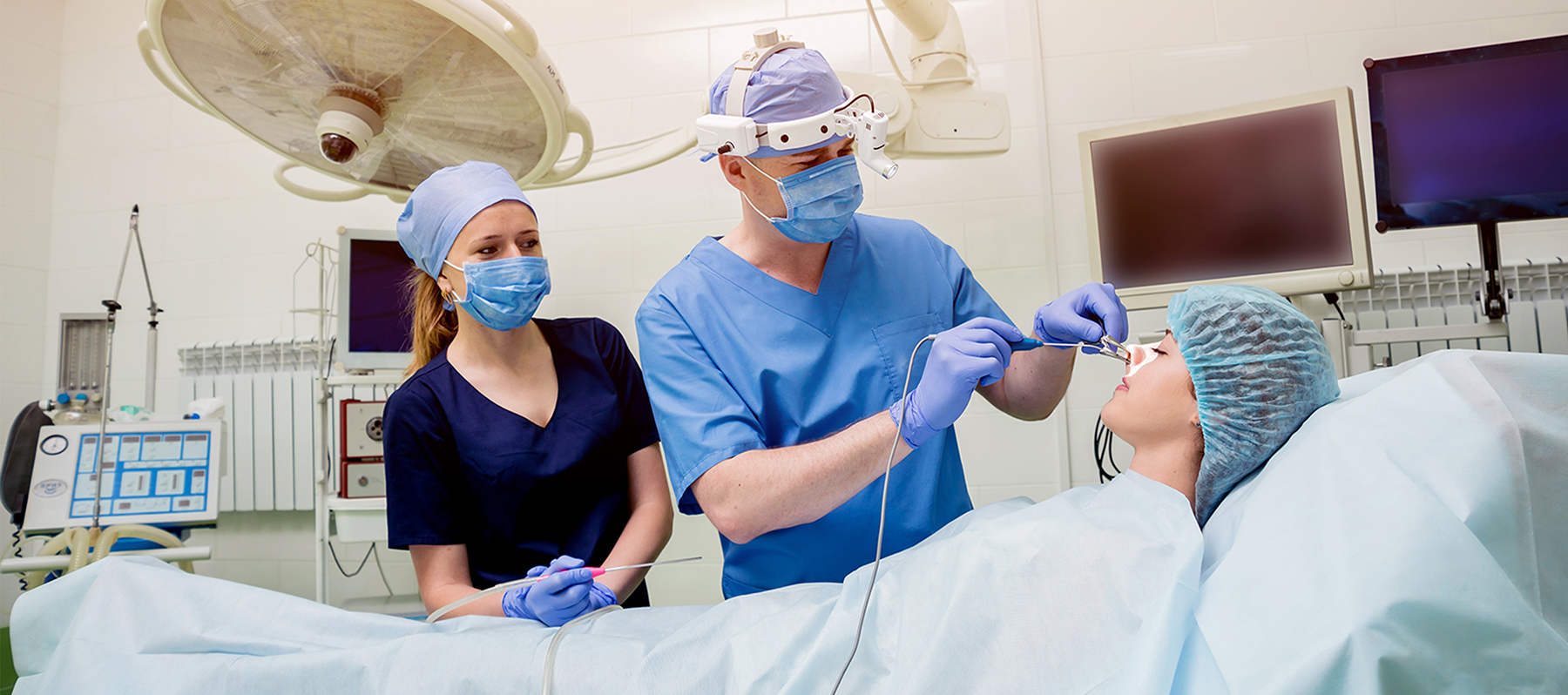 A male Keck Medicine surgeon in blue gear and an assistant perform sinus surgery on a female chronic sinusitis patient
