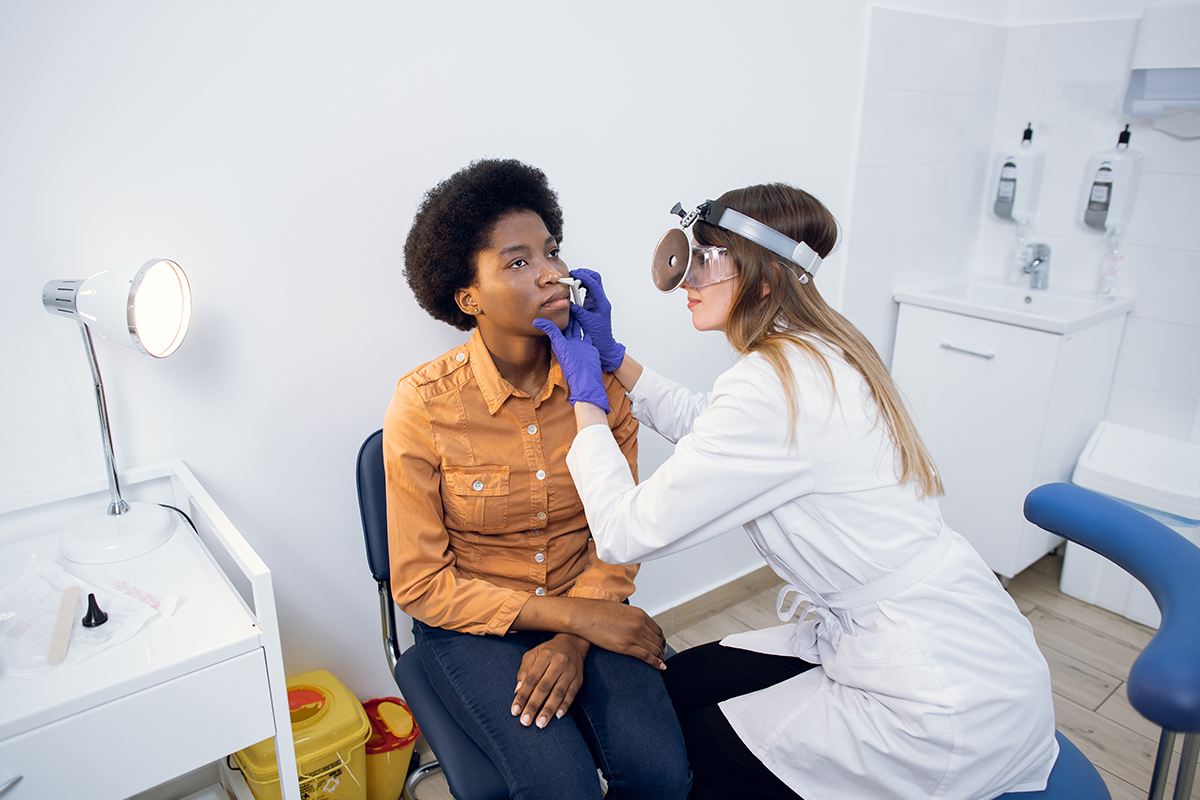 A female Keck Medicine sinus specialist wearing a head lamp and blue gloves treats a young female sinusitis patient