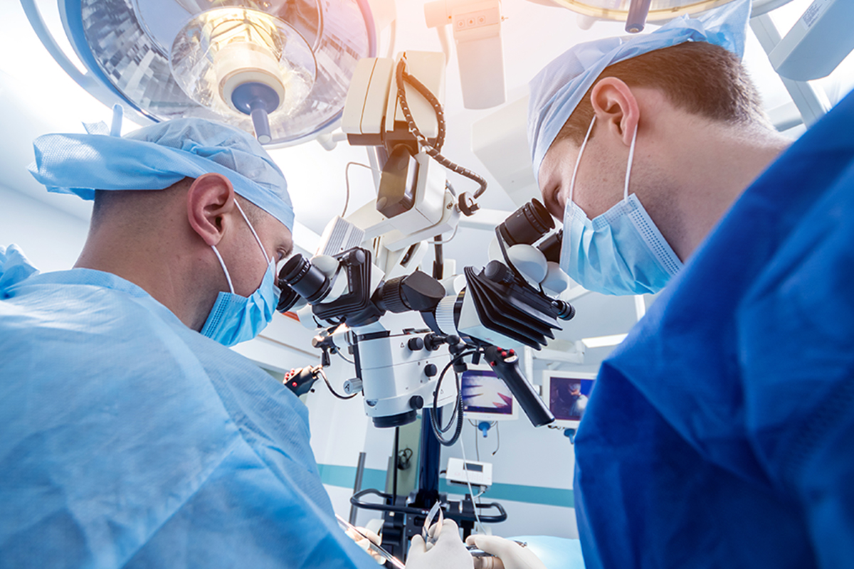 Two male Keck Medicine experts in Alzheimer's disease and other neurological problems look into a microscope during surgery