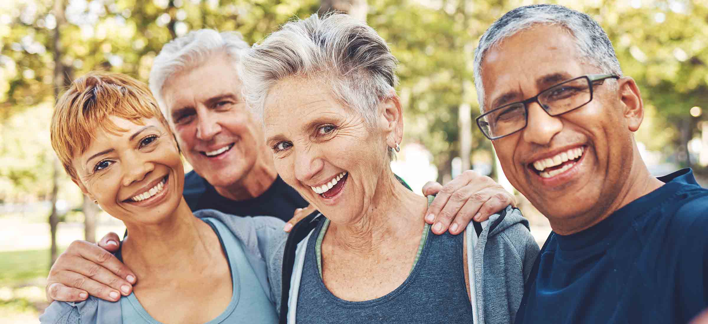 A group of elderly men and women smile into the camera with their hands on each other's shoulders.