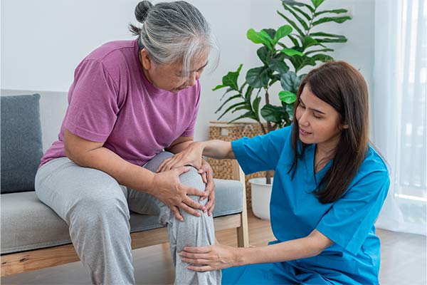 A doctor holds a patient's knee as she bends over on a couch.