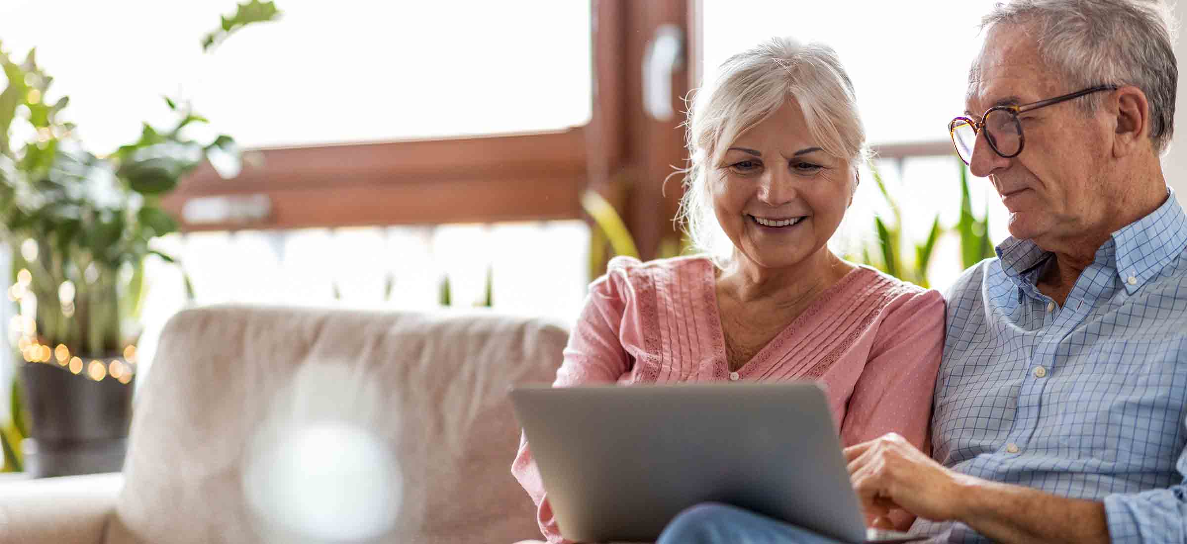 A man and a woman smile while sitting on a couch looking at a laptop.