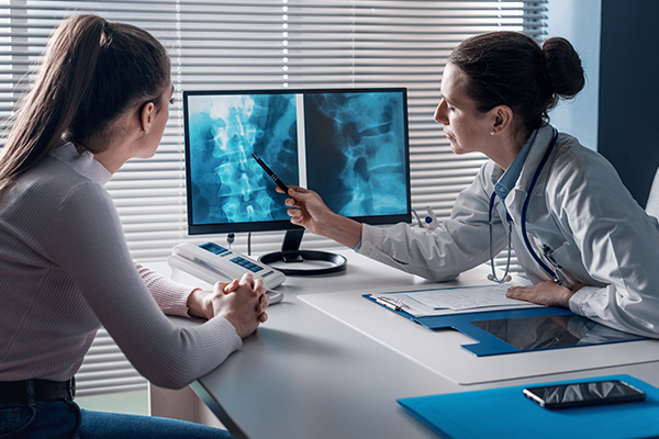 A doctor checks a patient's x-ray of spine at a table.