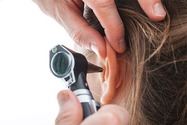 A doctor holds an instrument up to a patient's ear.