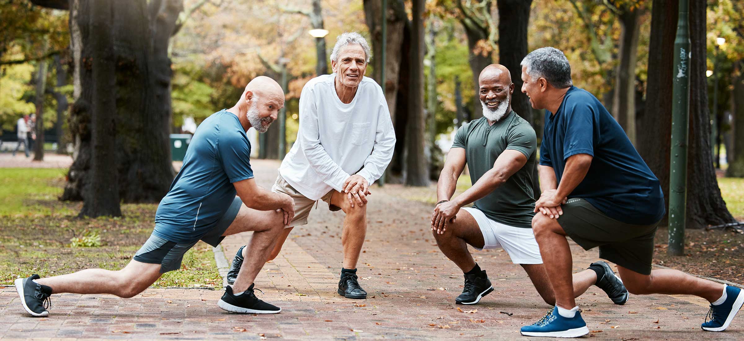 A group of elderly men stretch their knees on a trail in a park.