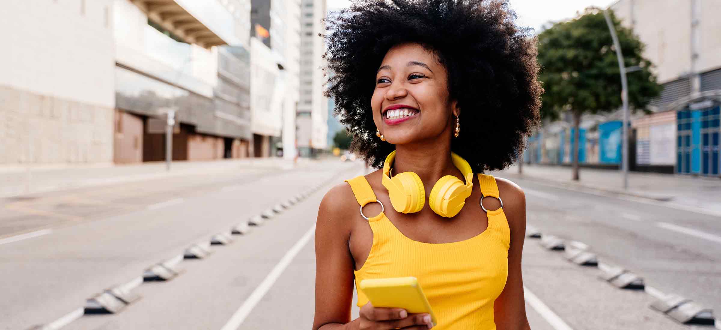 Beautiful young happy Black woman with curly hairstyle strolling in the city.