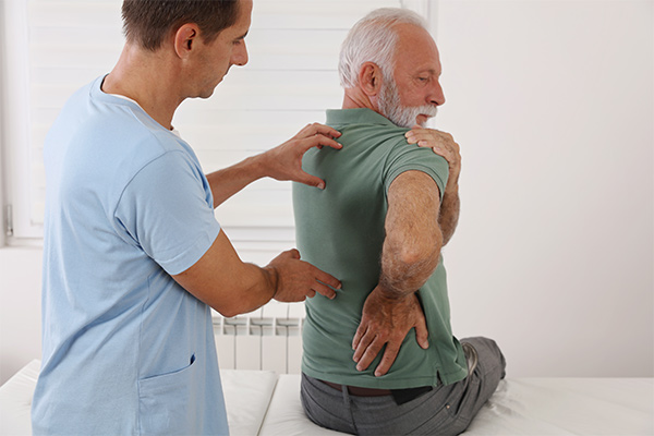 Spine clinician touches a male patient's back as he twists his head.