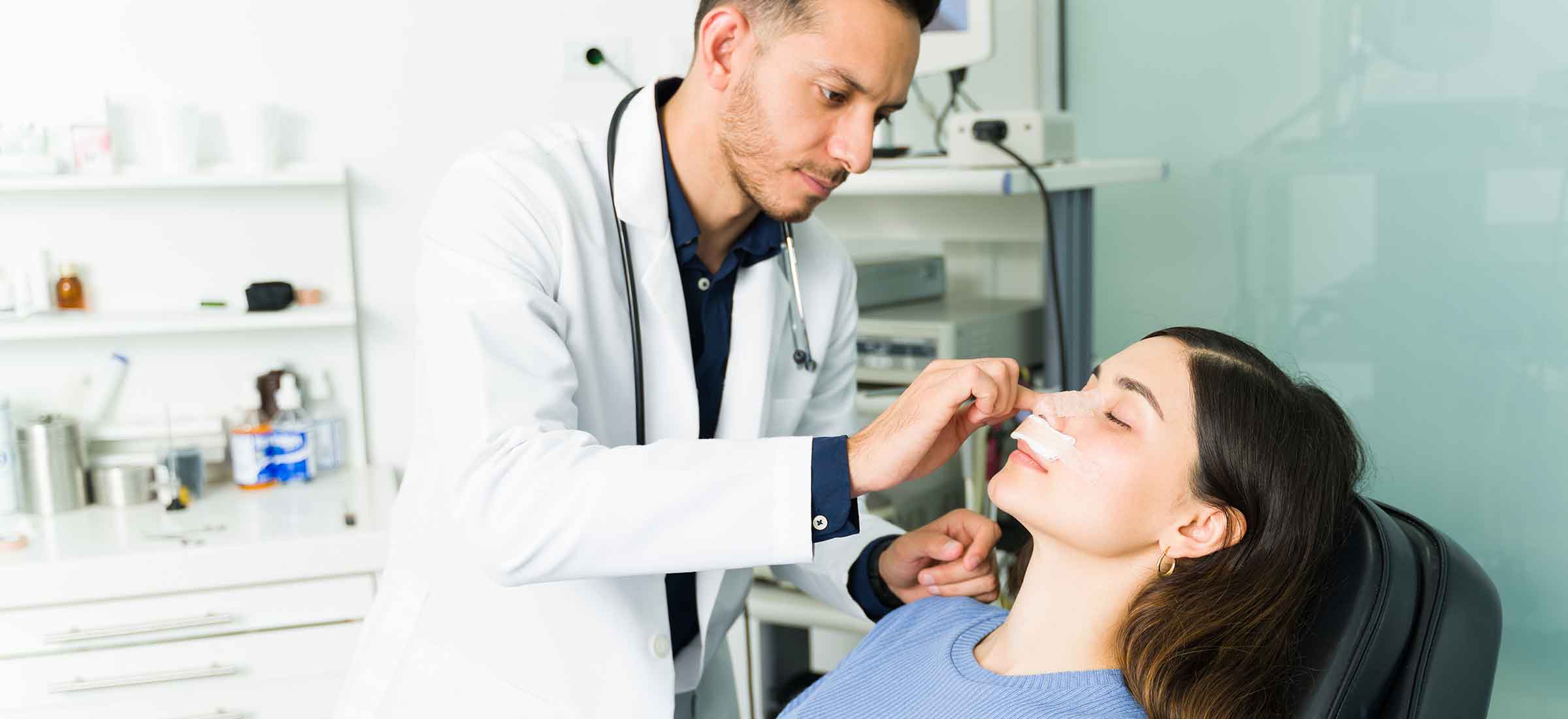 A doctor checks tape on a woman's nose.
