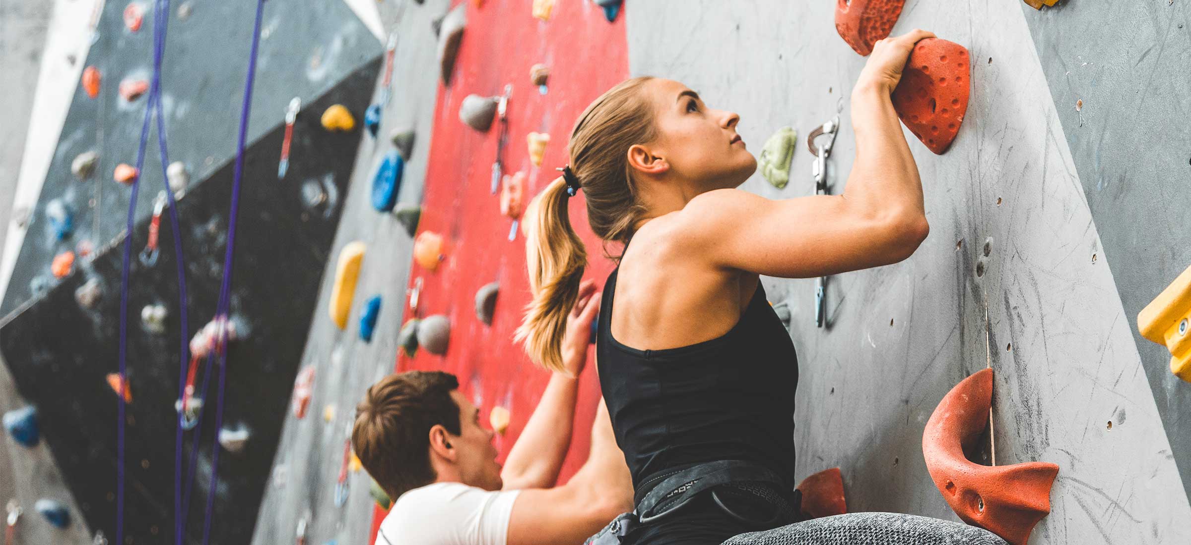 A woman climbs a rock climbing wall in a gym next to a man.