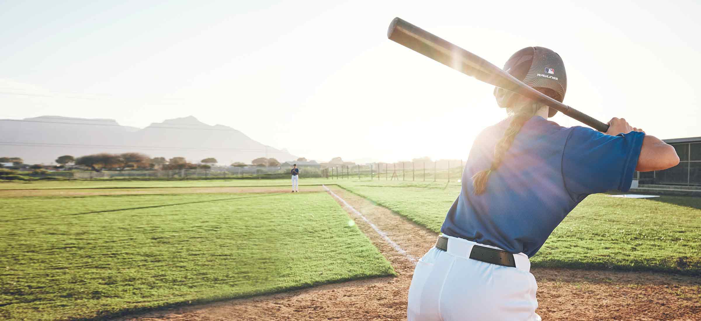 A softball player stands in a field with a bat in her hand ready to swing.