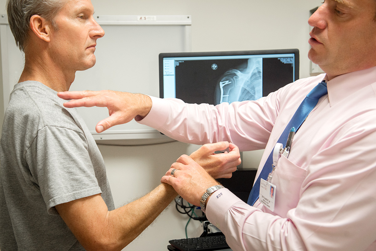 A male Keck Medicine orthopedic doctor examines a male patient's arm and shoulder rotator cuff tear by X-rays on a screen