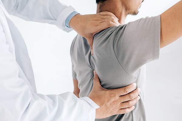 A doctor touches a patient's shoulder as they hold their arm in the air.