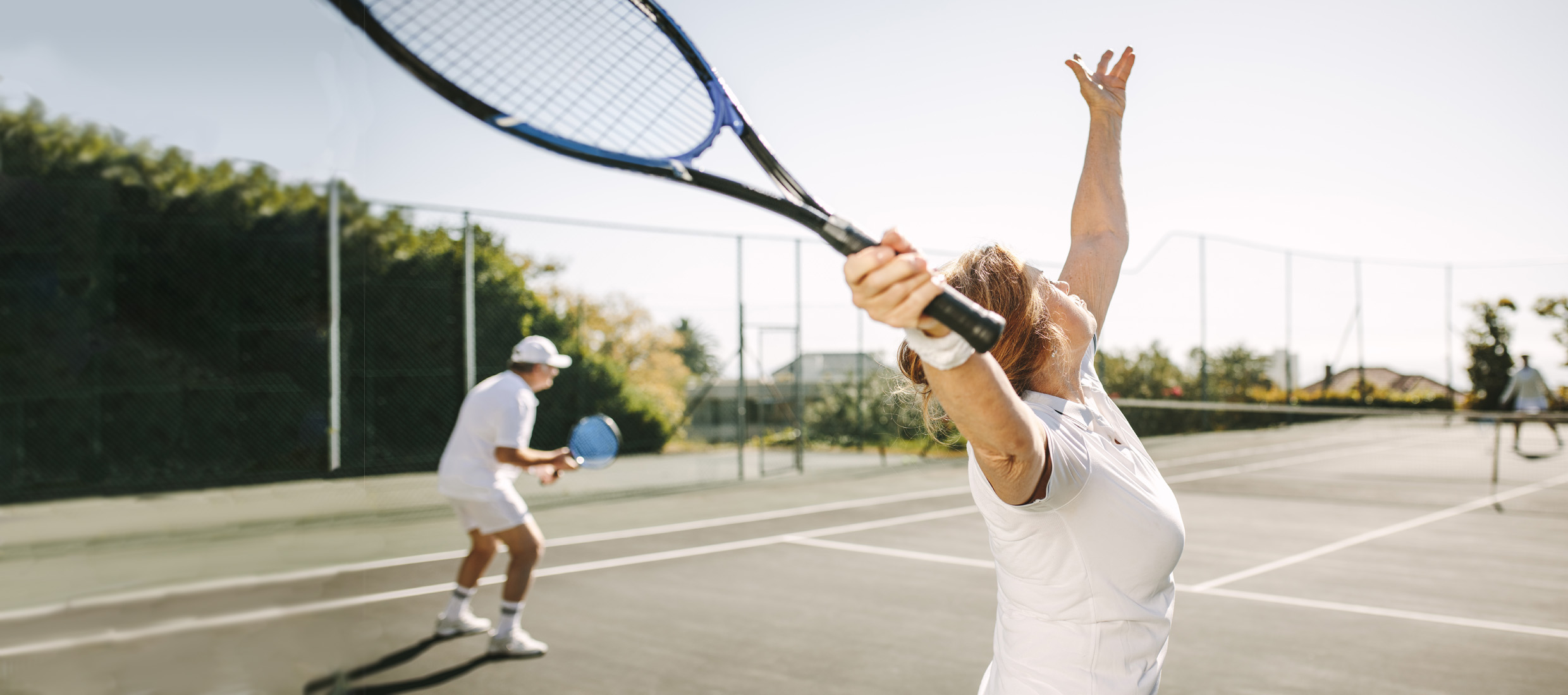 A female frozen shoulder patient with shoulder pain swings back a tennis racquet and outstretches her left arm