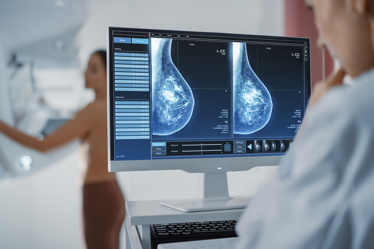 A female patient is screened for breast cancer, and a female Keck Medicine radiologist studies mammogram results on a screen