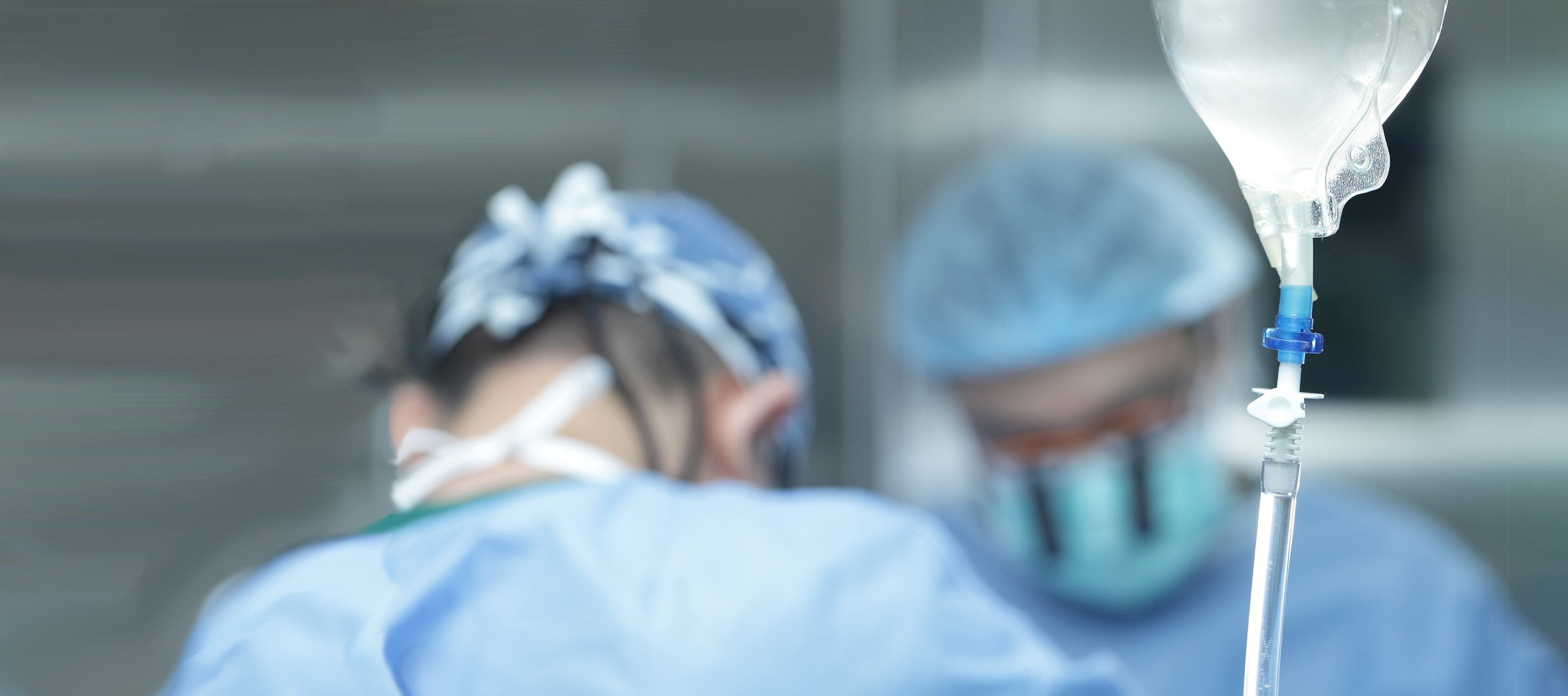 Two Keck Medicine blood cancer experts in blue gear perform a bone marrow transplant near an IV drip in an operating room