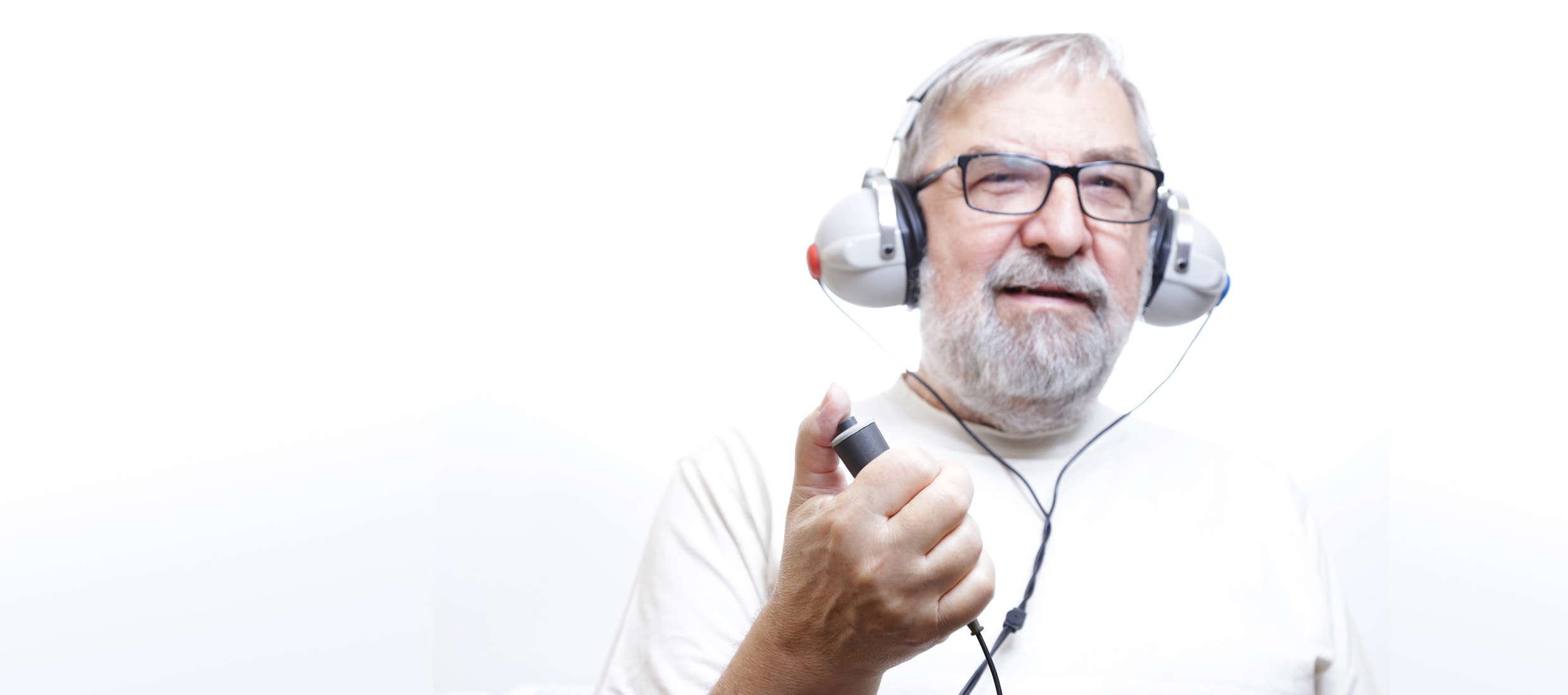 A male ossicular discontinuity patient wearing glasses has a hearing device over his ears and pushes a button with his thumb