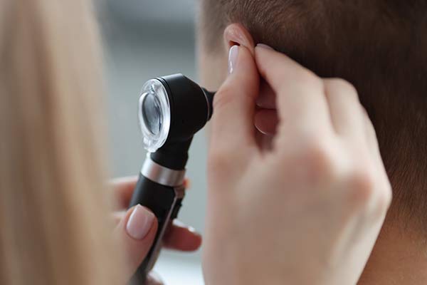 A doctor holds an instrument up to a patient's ear.