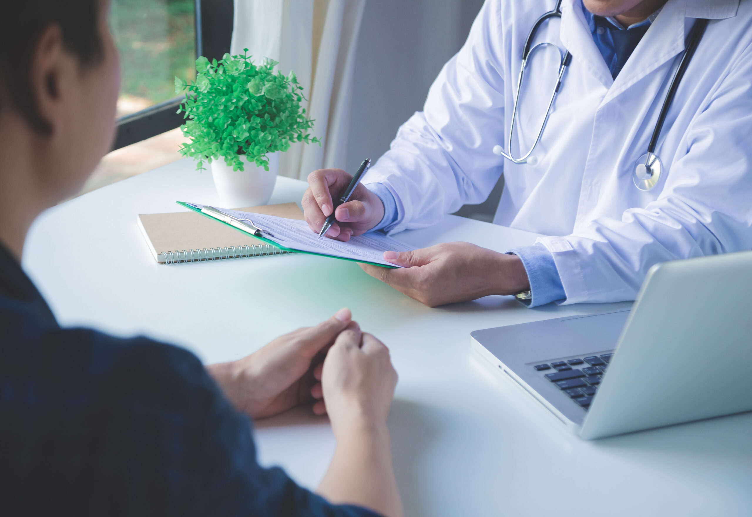A Keck Medicine urologist sits at a desk with a laptop and a plant and discusses causes of testicular cancer with a patient