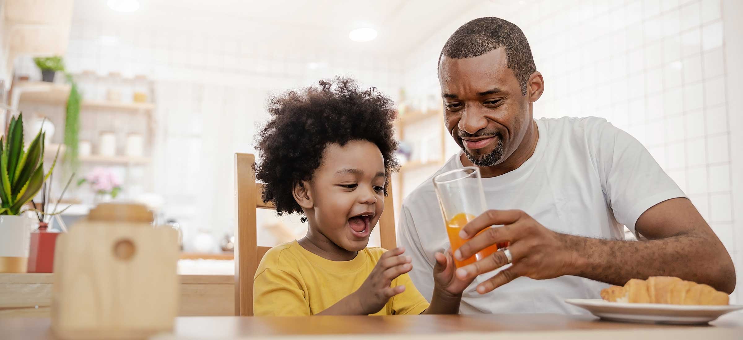 A man and son drink juice at a table.