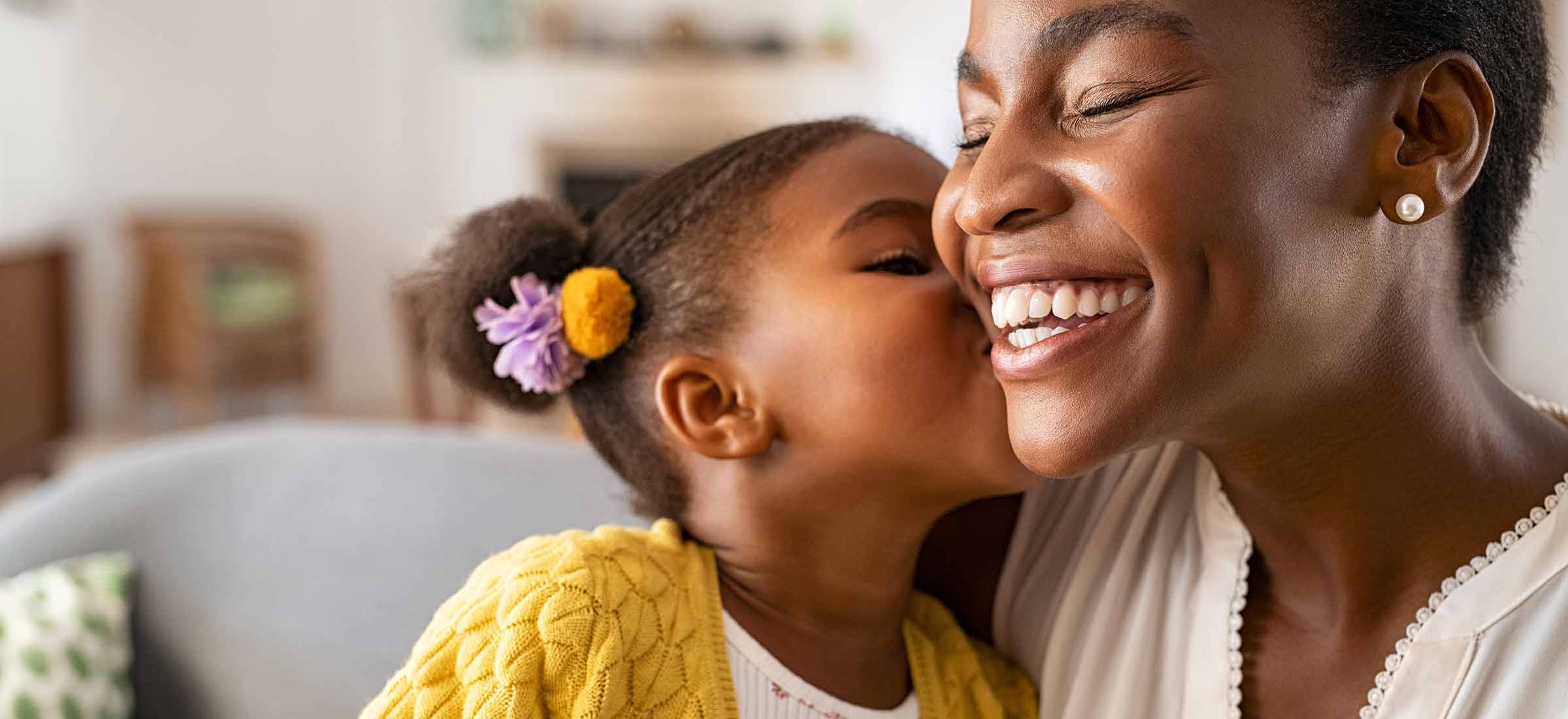 A girl kisses her mother on the cheek while sitting on a couch.