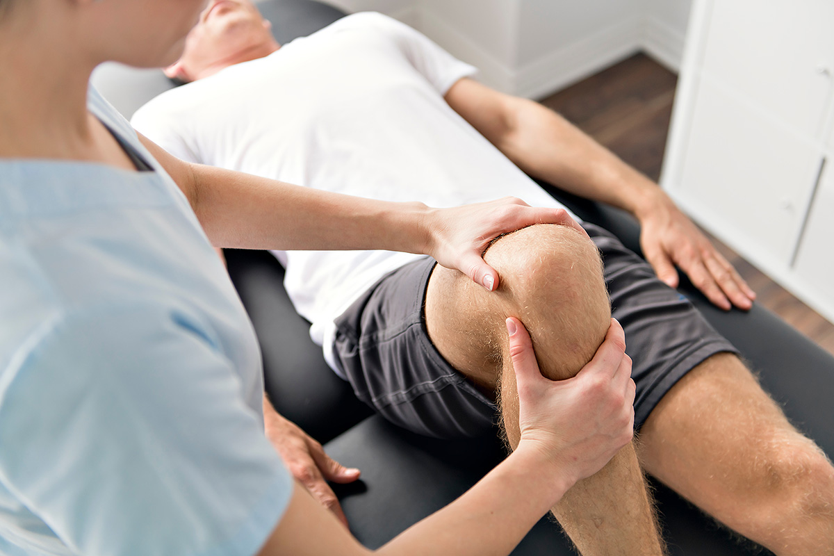 A male torn ACL patient lies on his back, while a Keck Medicine specialist performs physical therapy on his right knee