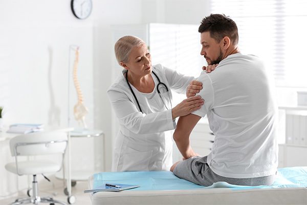 A doctor touches a patient's shoulder as he sits on a medical table.