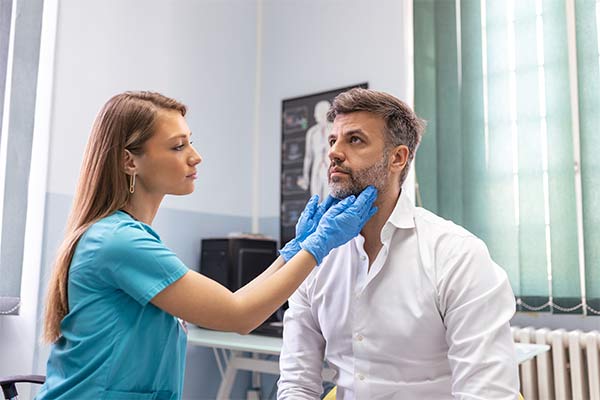 A doctor touches a.male patient's throat.