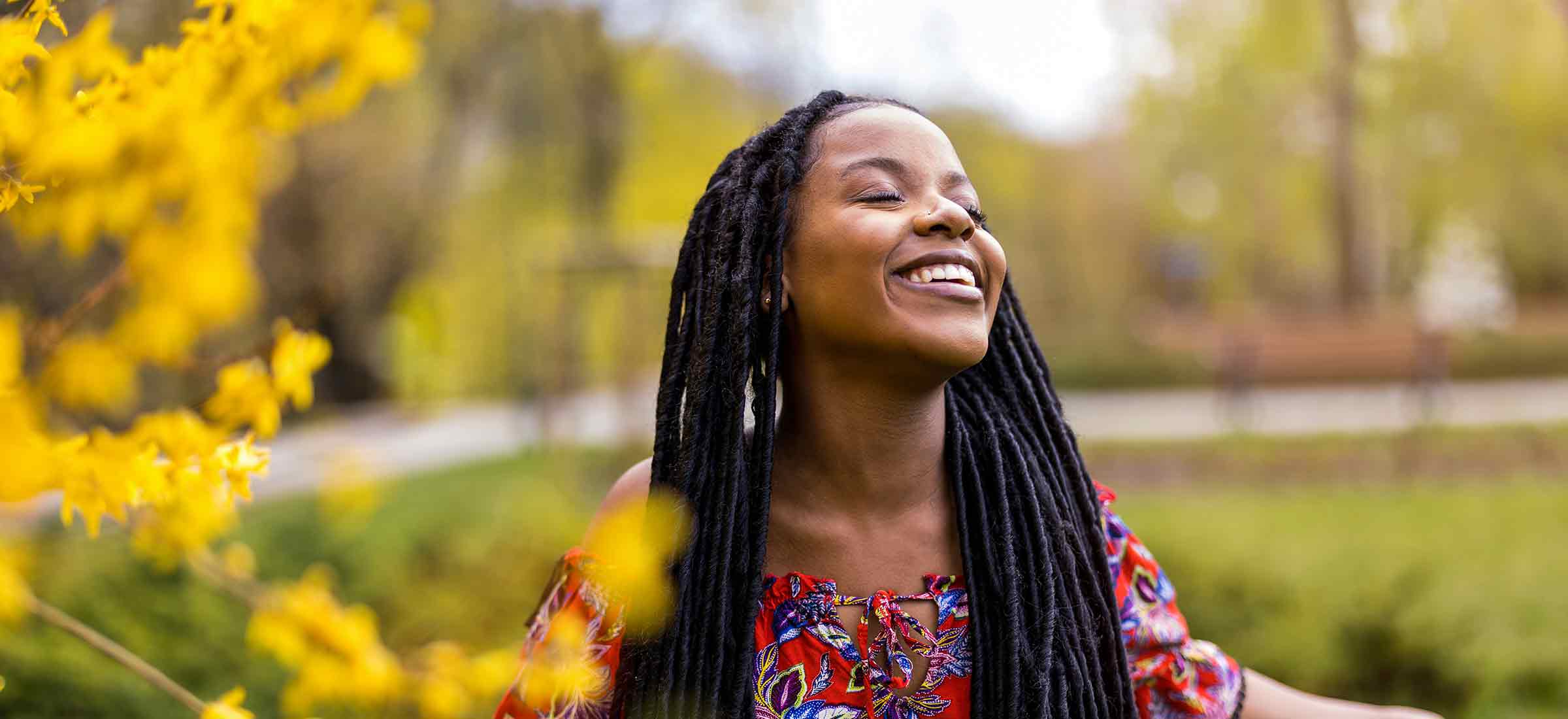 A woman smiles into the sky framed by yellow flowers in a park.