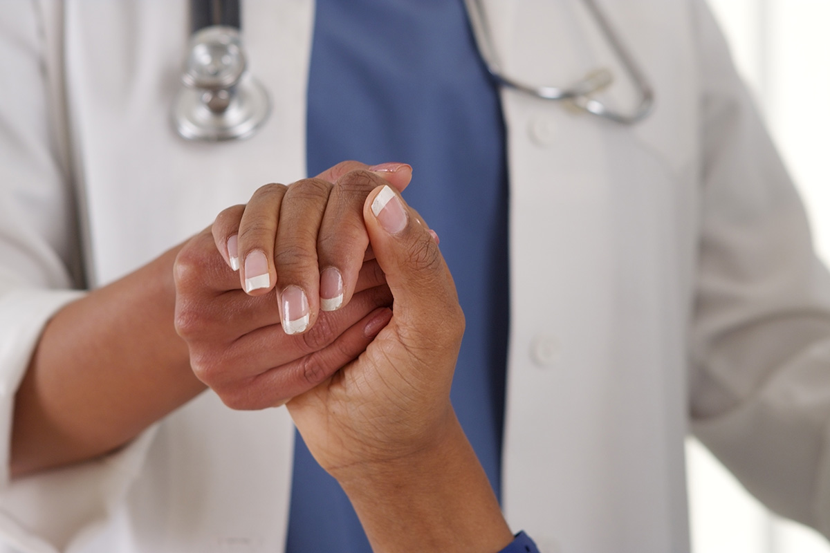A female Keck Medicine positive care specialist holds the hand of an HIV-positive patient who has French tip nail polish