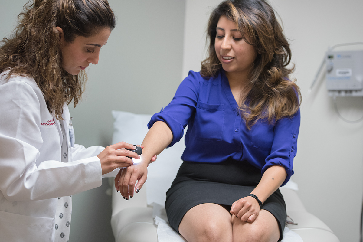 Keck Medicine of USC physician examines the skin of a female patient's hand and arm