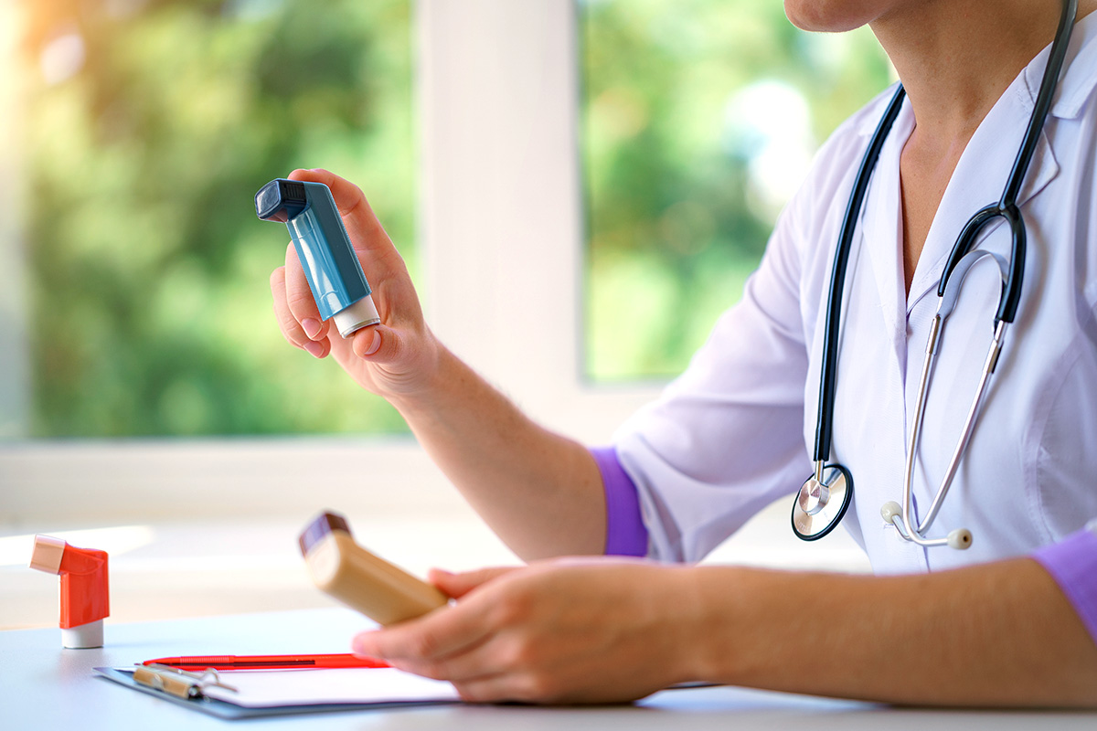A Keck Medicine of USC asthma specialist has a stethoscope around their neck, a chart on the table and holds an inhaler