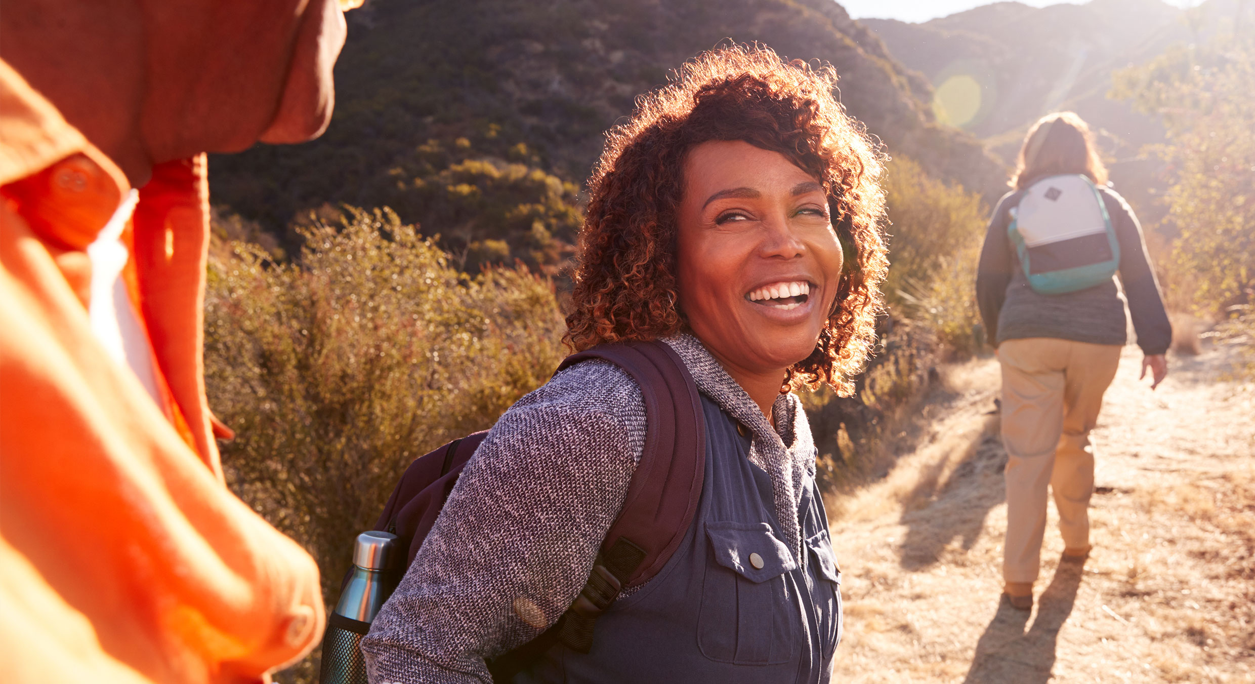 Woman smiling while hiking up a trail. Other hikers are visible in the background.