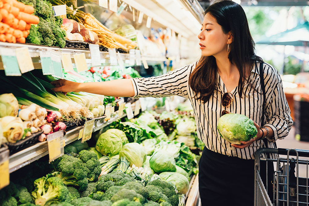 Woman holding a head of lettuce while shopping in the produce aisle of a grocery store