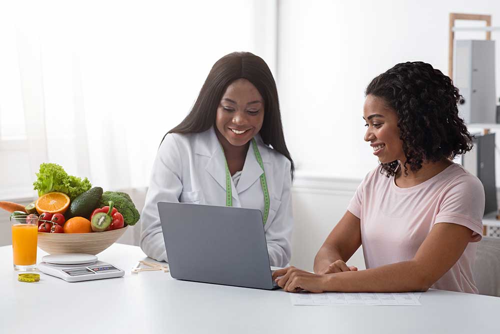 A dietitian and patient sit together in an office and review information on a laptop