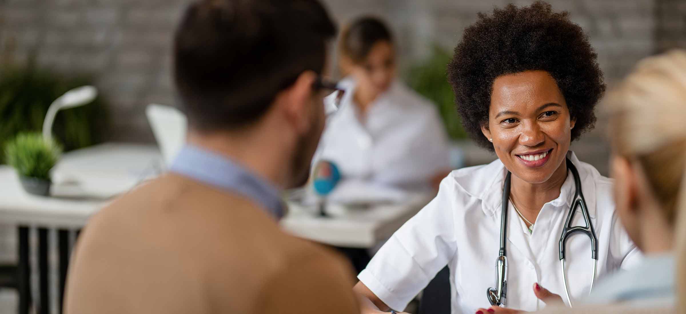 Happy doctor talking to a couple during consultations at clinic.